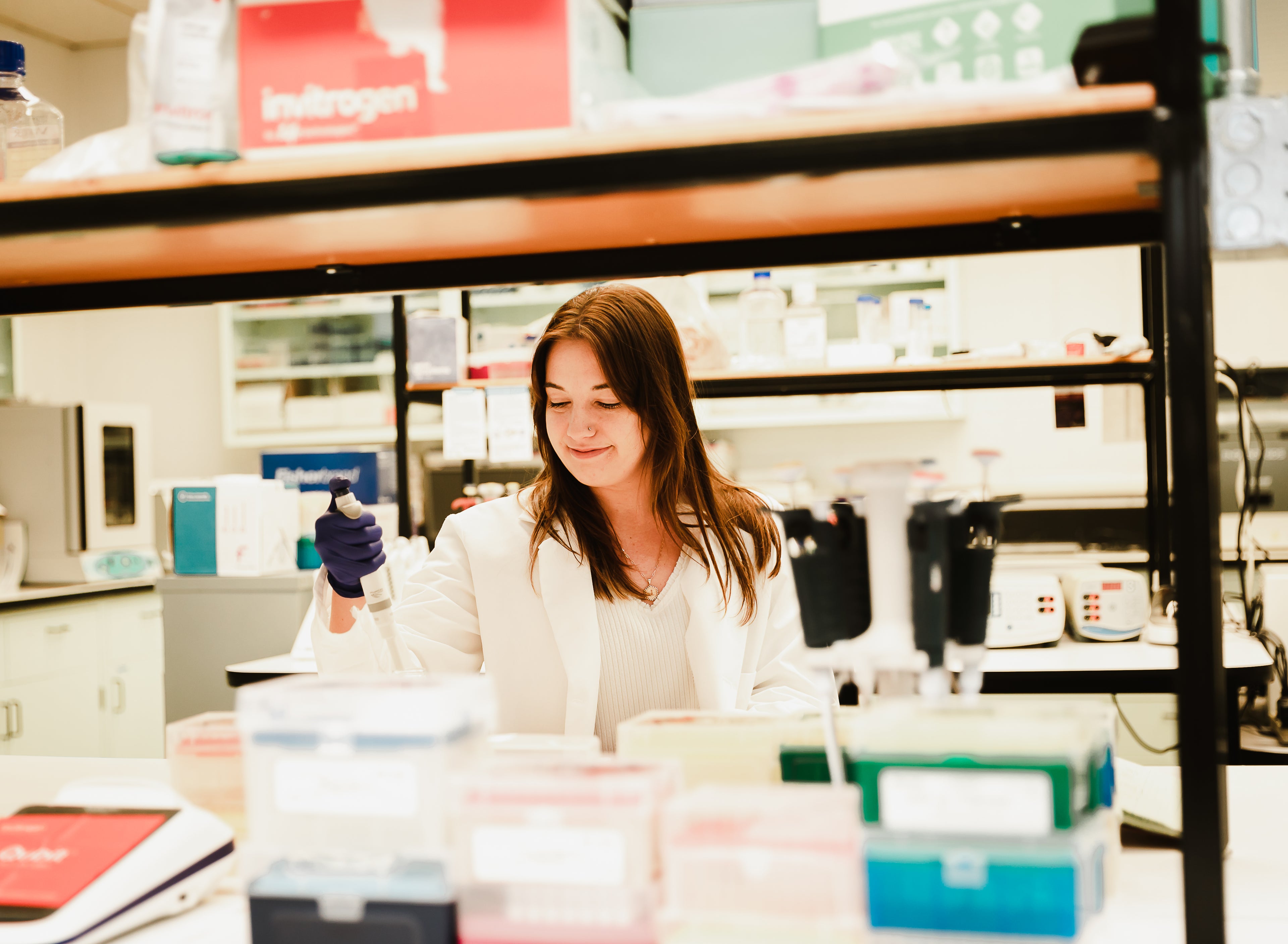 A woman in a laboratory holding a pipette with lab equipment around her.
